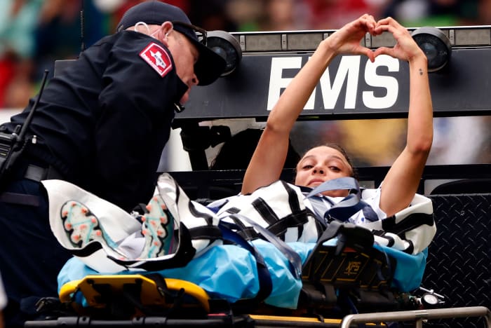 USWNT player Mallory Swanson holds her hands up in the shape of a heart as she is stretchered off the field.